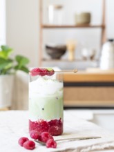 Raspberry matcha latte with ice, foam, fresh raspberries, and matcha powder on a counter