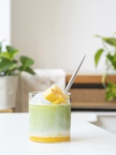 Iced matcha latte with tropical mango, milk, and clear straw in a glass