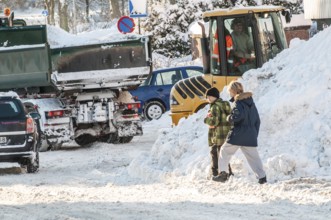 Two children playing among cars and loaders clearing snow on streets in Ystad, Skåne County,