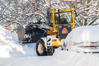 Loader clearing snow among snow-covered cars on streets in Ystad, Skåne County, Sweden, Scandinavia