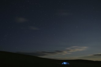 Illuminated tent stands alone in Mongolian steppe under starry sky at night, Nömrög National Park,