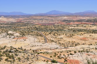 Curving road through dry, hilly landscape with reddish rocks under blue sky, Grand Staircase