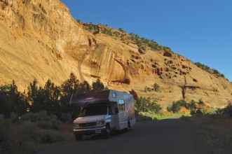 An RV parks on a road in a sunny rocky landscape with deep shade, Grand Staircase Escalante