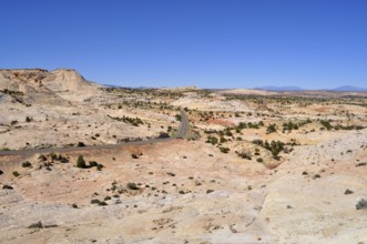 Paved road winds through dry landscape with reddish hills and sparse vegetation, Grand Staircase