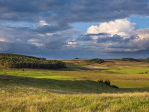 Hilly landscape in the Zicker Mountains in evening light under dramatic stormy clouds, including