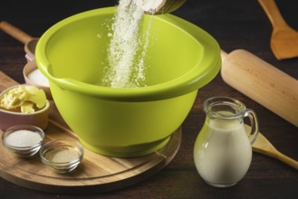 Flour falls into a green bowl surrounded by baking ingredients