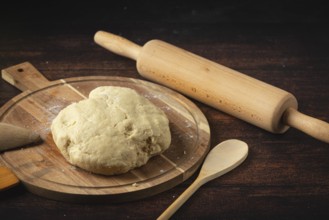 Fresh dough on a wooden table, ready to roll out, with a rolling pin