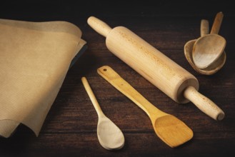 Rolling pin, cooking spoon and baking paper on a dark wooden table in a rustic atmosphere