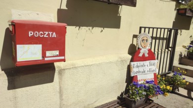 Red mailbox and doll decoration with flowers in sunny surroundings, Masuria, Poland