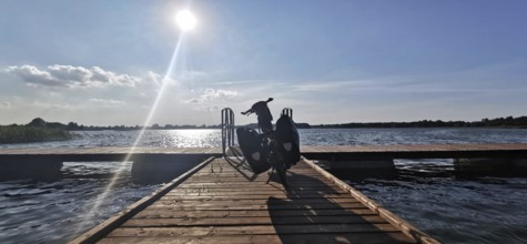 A bicycle is parked on a jetty leading out to the sunny lake, Masuria, Poland