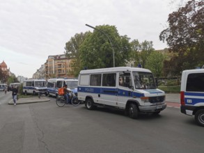 Several police vehicles on a city street, surrounded by buildings and trees, on the sidelines of