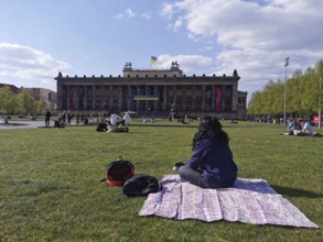 A woman sits on the meadow in front of the old museum on Museum Island in Berlin with the Ukrainian
