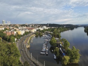View from above of a district of Prague, on a river with boats, surrounded by green trees and