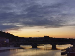 Dramatic orange sunset over the Vltava with silhouettes of Charles Bridge and Hradcany, Prague,
