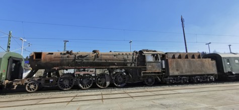 Transfer of a rusted historic steam locomotive on rails under clear blue skies at the train