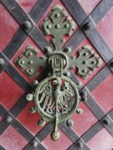 Decorative door knocker on red background decorated with coat of arms and metal ornaments, Poland