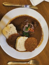 Delicious dish, Czech goulash on a plate with bread dumplings, meat garnished in sauce and onions,