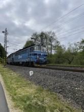 Blue train on tracks in a rural area under cloudy sky, Czech Republic