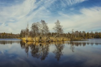 Calm lake with trees and clouds reflecting in the water. Autumn atmosphere with blue sky,