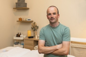 Male massage therapist owner standing with crossed arms in his wellness clinic, offering health,