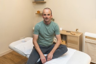Man sitting on a clean massage table in a modern wellness clinic, looking at the camera while