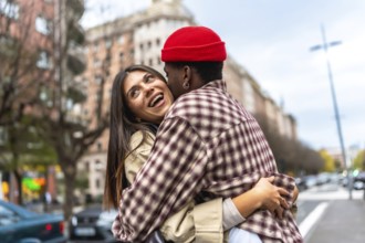 Young diverse couple embracing and laughing together on an urban street, sharing a moment of