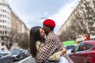Happy diverse couple embracing outdoors, a man kissing his smiling girlfriend's forehead on a city