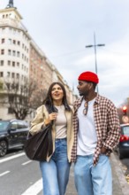 Young interracial couple walking arm in arm on a city street, smiling and talking as they enjoy