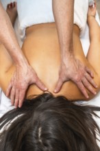 Therapist hands applying pressure to a woman's shoulders and upper back while she is lying on a