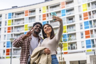 Happy diverse couple smiling and posing for a smartphone selfie, showing a peace sign while