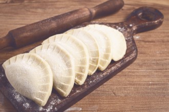 Raw chebureks, mini, on a cutting board, wooden table, close-up, no people