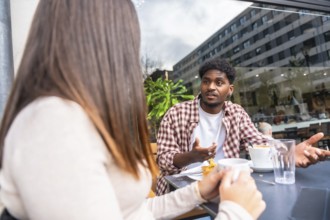 Young man and woman sit at an outdoor cafe in the city, sharing coffee and a serious conversation