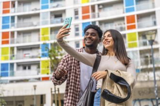 Happy young multiracial couple smiling, taking a selfie with a mobile phone in a vibrant urban