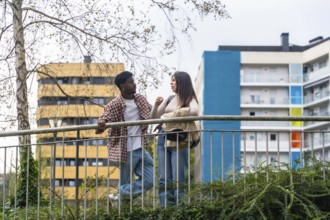 Two young adults, african american man and caucasian woman, chatting and leaning on a metal railing