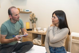Male physiotherapist attentively listening to a female patient on an examination table, who is
