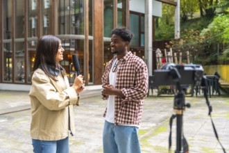 Female reporter holding a microphone, interviewing a smiling young african american man outdoors
