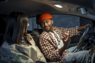 Young man wearing a beanie and plaid shirt talking to a woman passenger in a car during a night