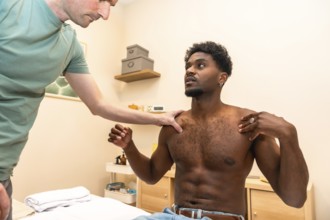 Male physiotherapist examining a young adult patient's shoulder and upper body, assessing mobility