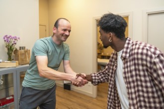 Two men from different backgrounds smiling and shaking hands in an office, symbolizing friendly