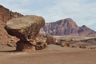 A gigantic rock sits on red desert sand in front of a barren rocky landscape, Grand Canyon National