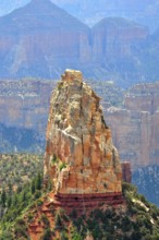 A massive rock rises steeply in a canyon landscape, surrounded by other rocks and sparse