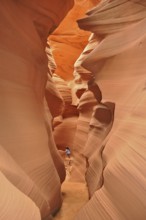 Person in a deep, wavy sandstone gorge with bright shades of orange, Antelope Canyon, Navajo Nation