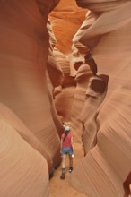 Person wandering through a narrow, winding canyon of orange sandstone, Antelope Canyon, Navajo