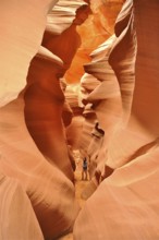 A traveler explores the narrow, winding passages of an orange slot canyon, Antelope Canyon, Navajo