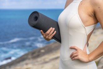 Woman standing outdoors holding a rolled yoga mat, preparing for a wellness and fitness session by