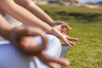 Woman forming a meditative mudra with hands while seated on green grass, focusing on inner peace,