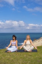 Two women sitting on yoga mats in a lotus position with eyes closed, finding tranquility and