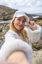 Happy woman smiling to camera and adjusting her white cap, enjoying a casual outdoor moment on a