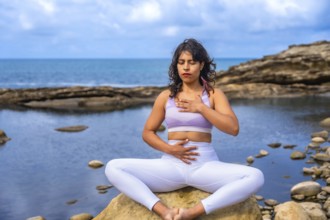 Woman practicing mindfulness and holistic wellness, sitting in a meditative yoga pose on a rock at