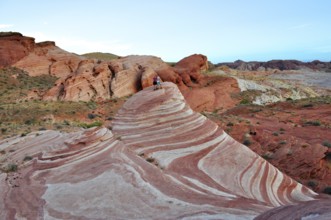 Two people standing on a striped rock formation in a desert landscape, Valley of Fire State Park,
